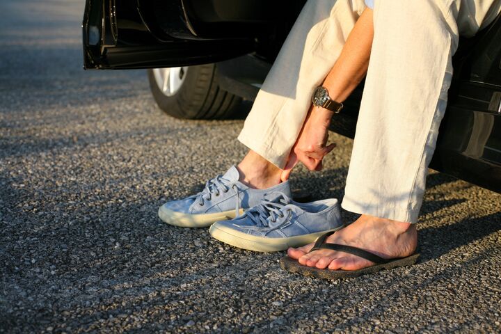 Eine Person wechselt im Auto sitzend ihre Schuhe von Flip-Flops zu bequemen und festen Straßenschuhen