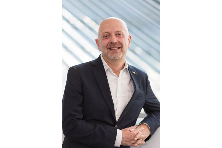 Portrait eines Mannes der am Geländer lehnt, einen weißes Hemd und einen schwarze Anzugjacke trägt.