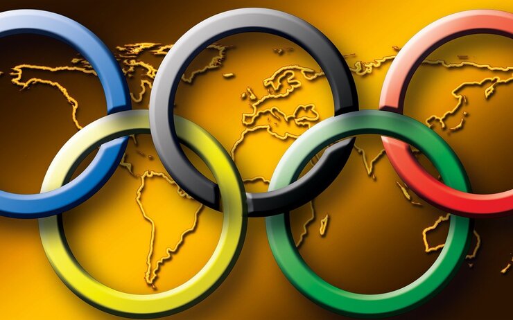 Die Olympischen Ringe vor einer goldenen Weltkarte.