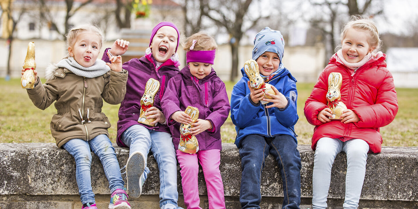 5 Kinder sitzen auf einer Mauer und halten Schokoosterhasen in der Hand auf Schloss Hof.
