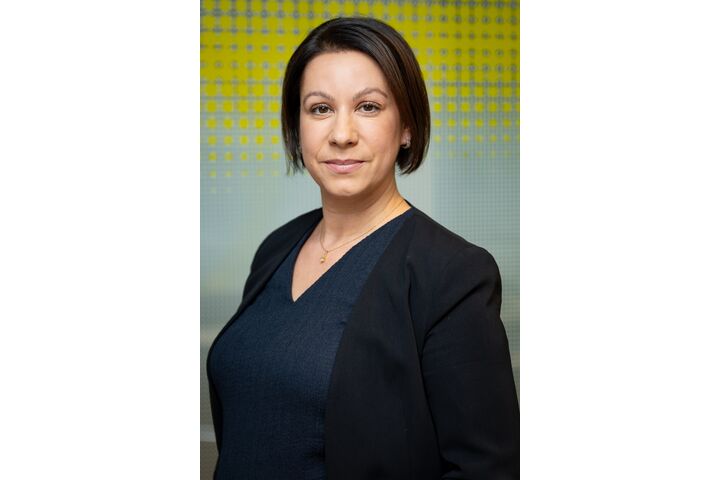 Porträtfoto einer Frau mit mittellangen braunen Haaren, die vor einer gelben-weißen Glaswand steht