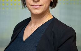 Porträtfoto einer Frau mit mittellangen braunen Haaren, die vor einer gelben-weißen Glaswand steht