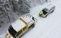 Ein ÖAMTC-Pannenfahrzeug schleppt ein anderes Fahrzeug in winterlicher Landschaft ab