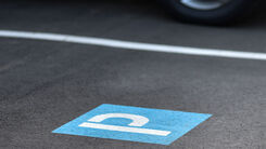 Kennzeichnung eines Parkplatzes mit dem Symbol P am Boden (weiß auf blauem Hintergrund) und weißer Randlinie; hinter der weißen Linie sieht man ein geparktes Auto.