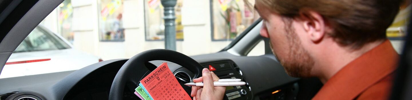Mann, der im Auto sitzend, einen Parkschein ausfüllt