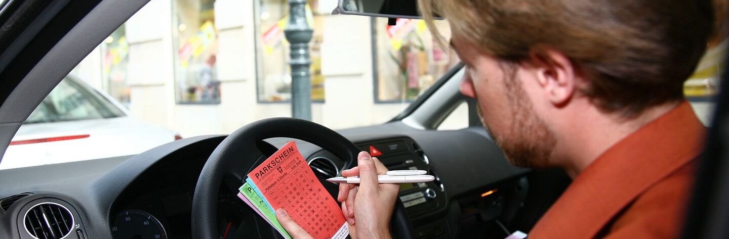 Mann, der im Auto sitzend, einen Parkschein ausfüllt
