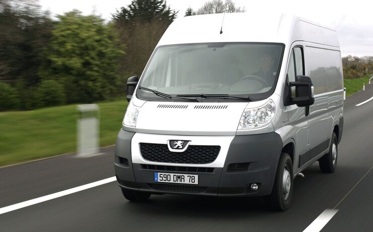 Das Bild zeigt ein weißes Nutzfahrzeug, welches auf einer Landstraße unterwegs ist.