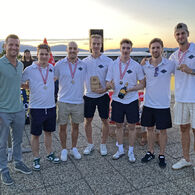 Im Bild zu sehen sind die Zweitplatzierten des Team Wolf bei der Siegerehrung, sie tragen eine Medaille um den Hals und halten einen Pokal und eine Flasche in die Kamera