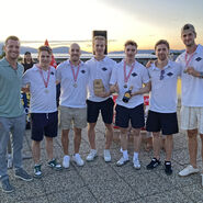 Im Bild zu sehen sind die Zweitplatzierten des Team Wolf bei der Siegerehrung, sie tragen eine Medaille um den Hals und halten einen Pokal und eine Flasche in die Kamera