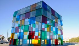 Das Foto zeigt den Eingang ins Centre Pompidou in Malaga, das die Form eines farbigen Würfels hat und aus zahlreichen bunten Quadraten besteht.