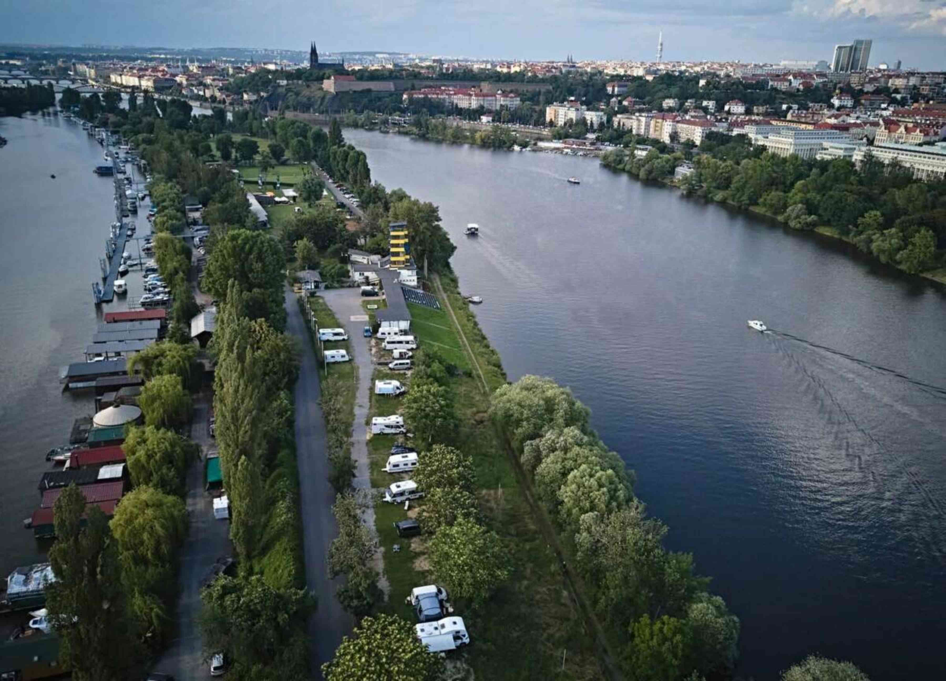 Ein Luftbild zeigt eine Flusslandschaft mit Campingplatz und Wohnmobilen entlang des Ufers.