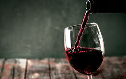 Es wird gerade aus einer Glasflasche Rotwein in ein Weinglas geleert.