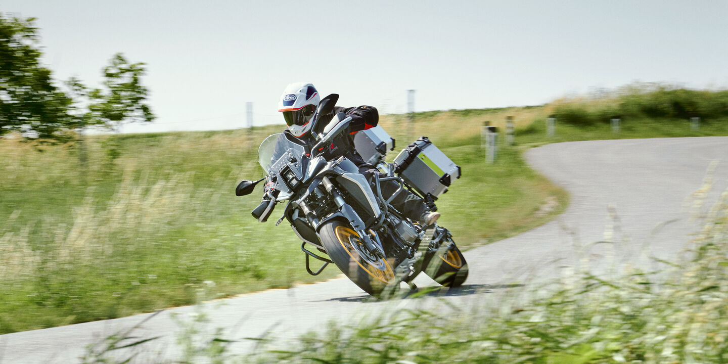 Die Reisenduro fährt in Schräglage eine Rechtskurve auf einer Landstraße entlang.