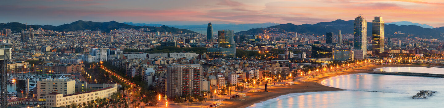 Beim Sonnenaufgang offenbart sich vom Küstenblick aus die faszinierende Skyline von Barcelona, die vom ersten Tageslicht erhellt wird und ein malerisches Panorama bietet