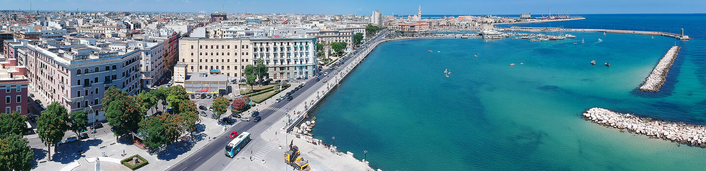 Ein weites Panorama zeigt die lebendige Stadt Bari mit ihrer historischen Altstadt, hellen Gebäuden und dem glitzernden Meer.