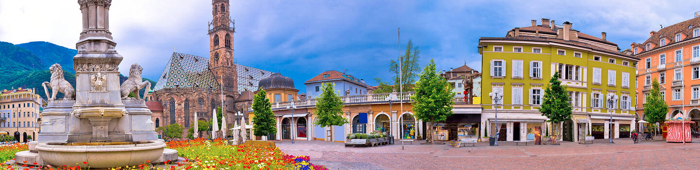 Ein lebendiger Blick auf den Waltherplatz in Bozen, mit bunten Fassaden der umliegenden Gebäude und der Statue von Walther von der Vogelweide, die stolz im Zentrum des Platzes steht.