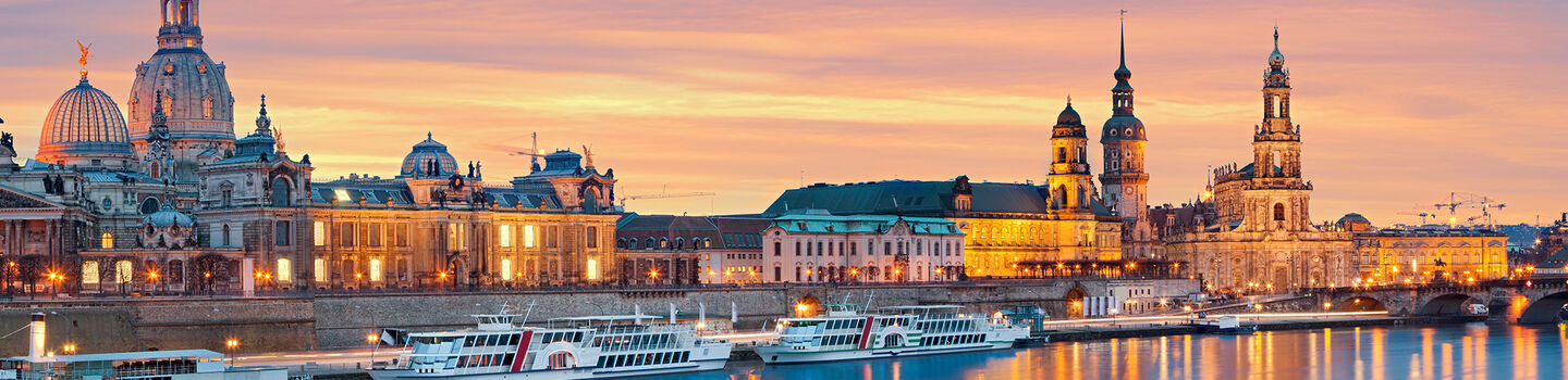 Sonnenuntergang über Dresden, mit dem Wasser, das die goldenen und orangefarbenen Lichter widerspiegelt, während die Stadt in eine ruhige Abendstimmung getaucht ist.