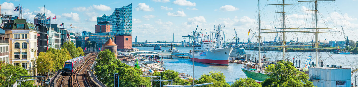 Hamburg mit den Landungsbrücken, der Elbphilharmonie und dem Hafen, unter einem klaren blauen Himmel.