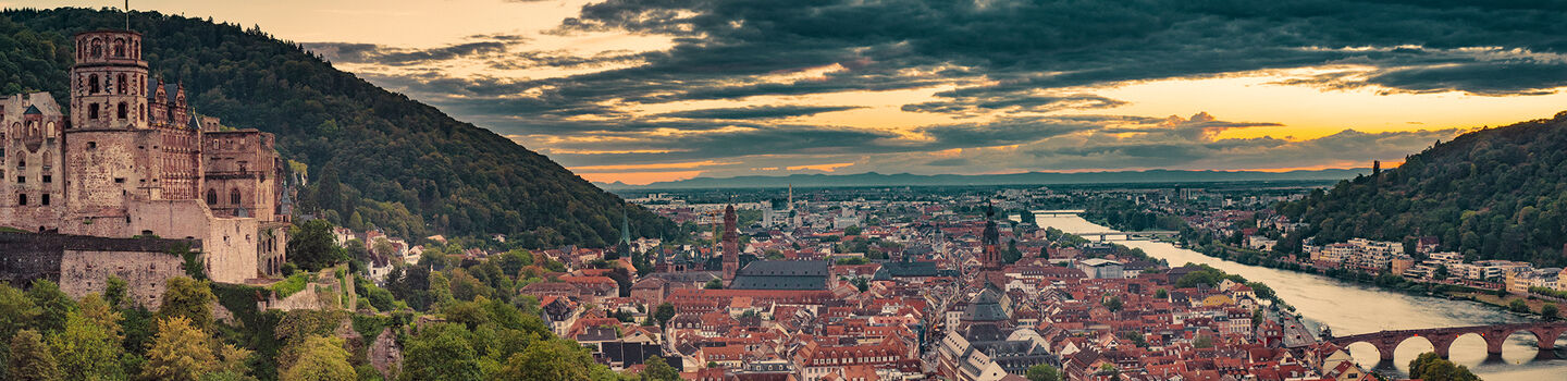 Panorama von Heidelberg in einer düsteren Abendstimmung, mit der Altstadt und dem Schloss, die in gedämpften, dunklen Farben unter einem wolkenverhangenen Himmel liegen.