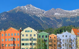 Die Häuserfassaden am Inn beeindrucken mit ihrer traditionellen Architektur und farbenfrohen Gestaltung, die eine attraktive Szenerie vor dem Bergpanorama schaffen.
