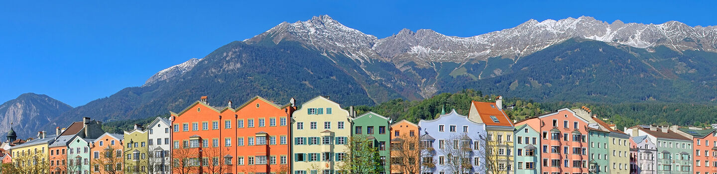 Die Häuserfassaden am Inn beeindrucken mit ihrer traditionellen Architektur und farbenfrohen Gestaltung, die eine attraktive Szenerie vor dem Bergpanorama schaffen.