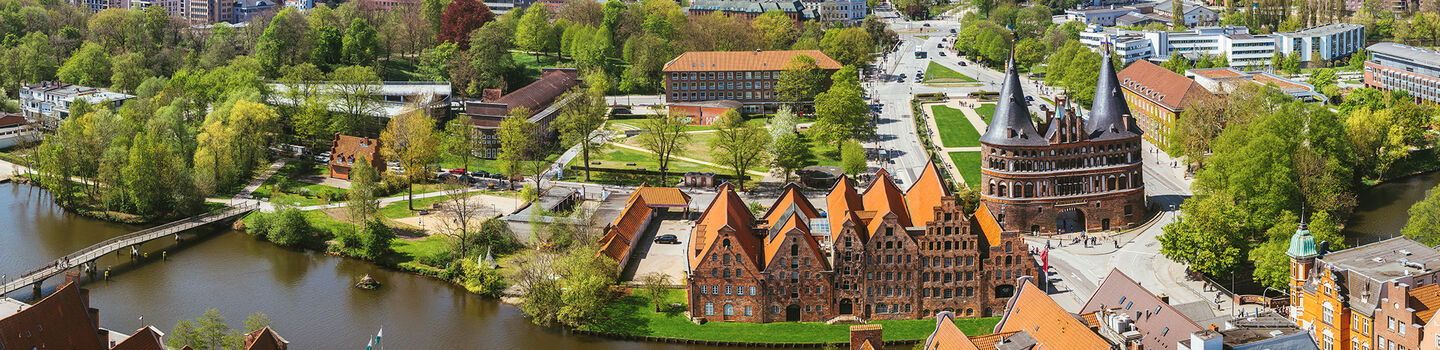 Das Holstentor in Lübeck aus der Vogelperspektive, mit den markanten roten Backsteinbauten, die sich gegen den klaren Himmel abheben.