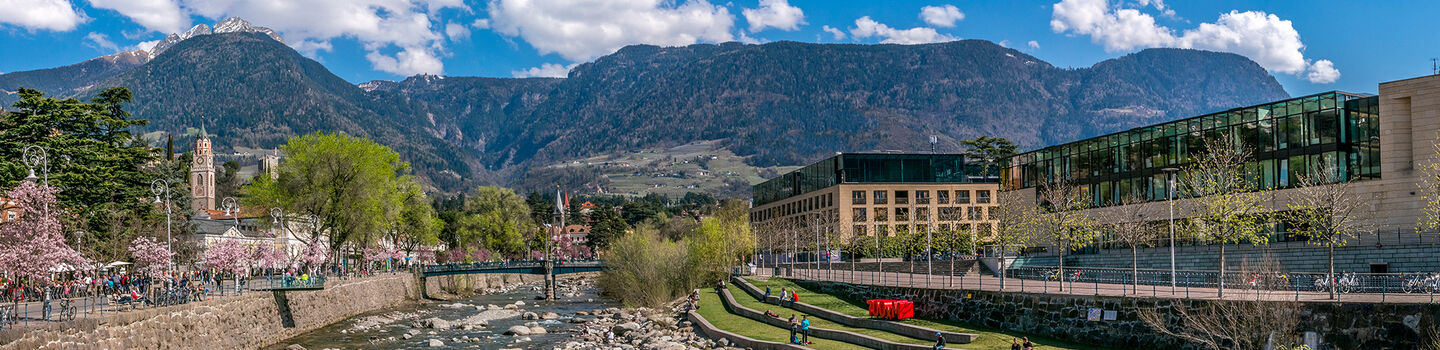 Blick auf die Passer in Meran im Frühling, mit dem ruhigen Wasser, das durch die Stadt fließt, und den modernen Gebäuden entlang des Flusses.