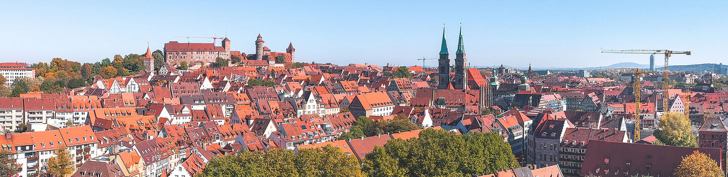 Panorama von Nürnberg, mit den charakteristischen roten Dächern der Altstadt, die sich unter einem klaren blauen Himmel erstrecken.