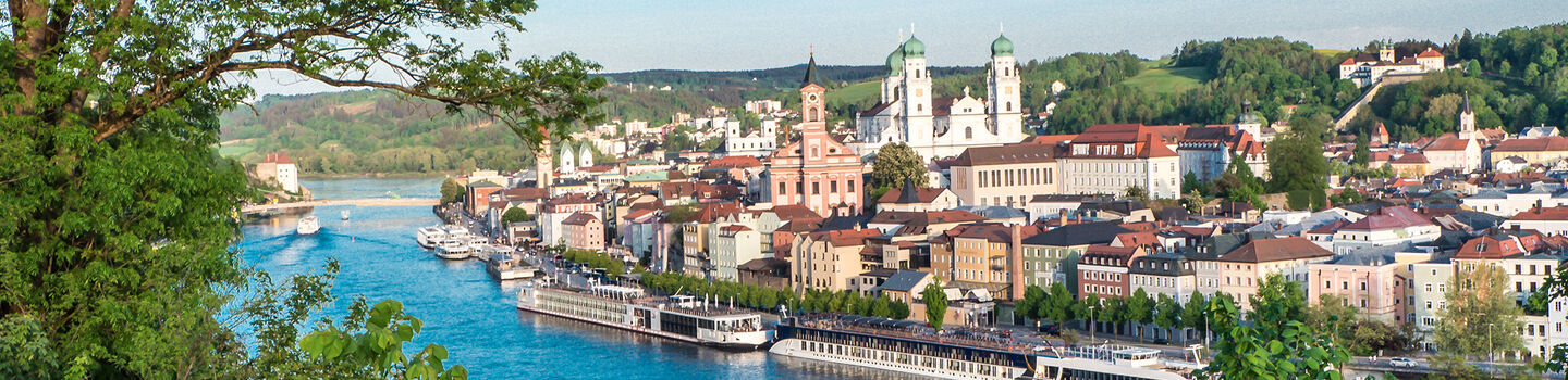 Blick auf Passau, mit dem leuchtend blauen Rhein, der sich durch die Stadt schlängelt und von Bäumen umgeben ist.