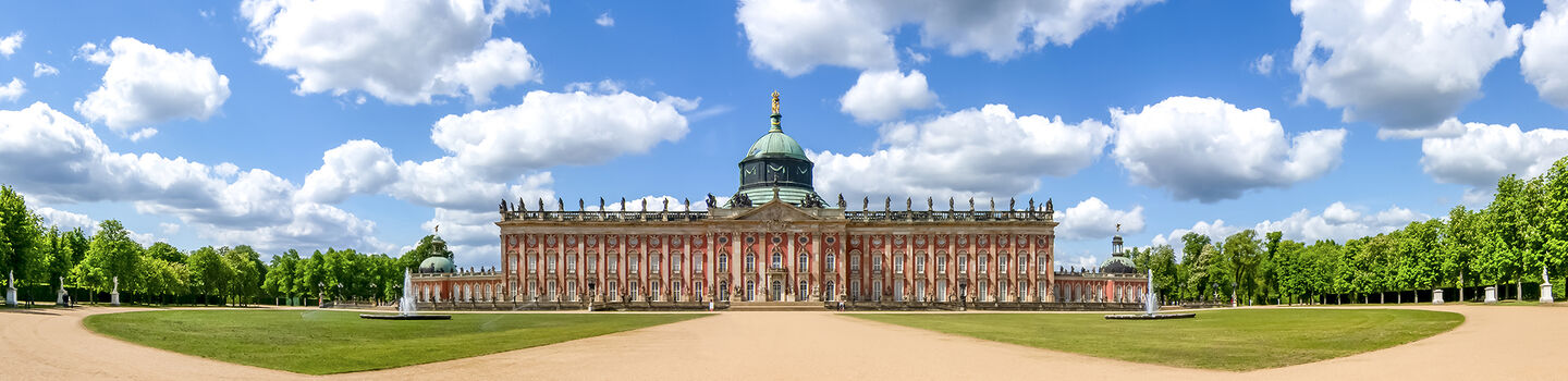 Das Neue Palais in Potsdam in der Frontalansicht, mit seiner herrschaftlichen Fassade, die unter einem klaren blauen Himmel erstrahlt.