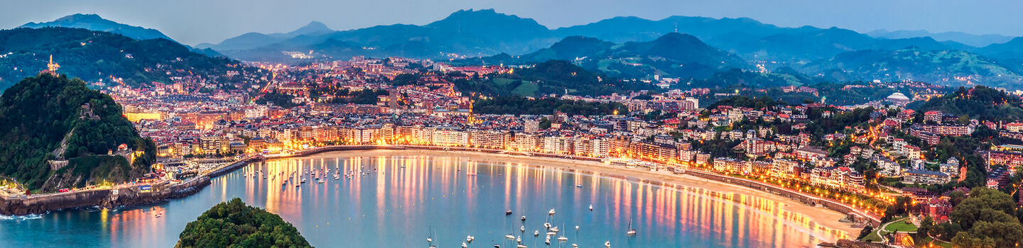 Mit dem Blick auf die Bucht wirkt San Sebastian in der abendlichen Beleuchtung magisch, während die zahlreichen Lichter der Stadt auf dem Wasser glitzern.