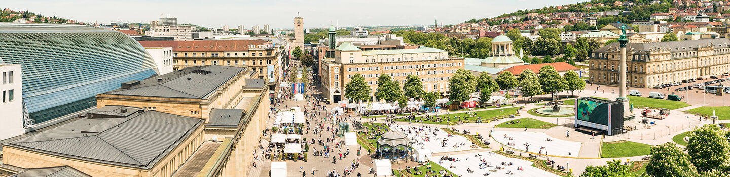 Schlossplatz in Stuttgart aus der Vogelperspektive, mit vielen Menschen, die sich auf der weiten Fläche bewegen, umgeben von den umstehenden Gebäuden.