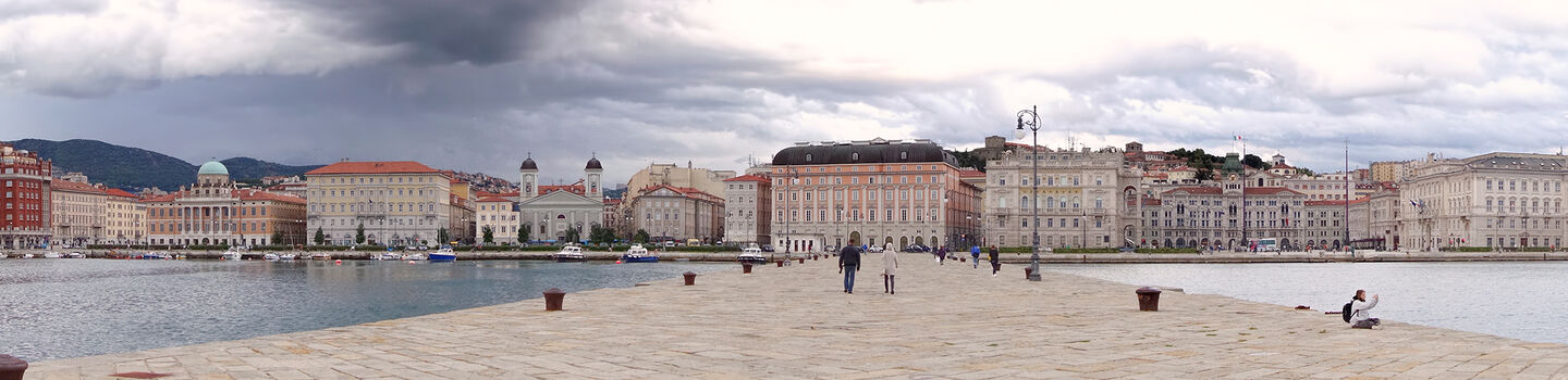 Unter einem trüben Himmel erstreckt sich das historische Molo Audace von Triest in das ruhige, graue Meer.