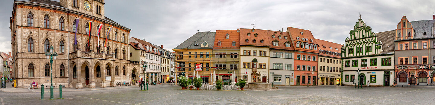 Der Alte Marktplatz in Weimar, mit bunten historischen Gebäuden, die sich unter einem grauen, wolkenverhangenen Himmel erstrecken.