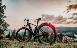 E-Mountainbike, abgestellt auf einer Bergwiese bei Sonnenuntergang mit Blick ins Tal.