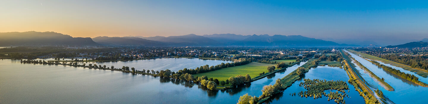 Die Sonne geht sanft über den Bergen hinter dem Bodensee auf und spiegelt sich dabei im See. 