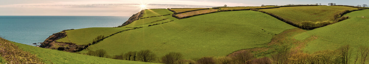 Grüne Wiesen und Hügel in Cornwall, Blick aufs Meer im Hintergrund iStock.com / Sabine Wagner