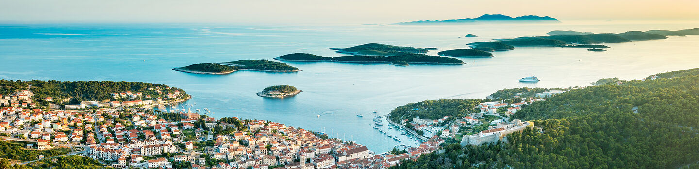 Die Stadt Hvar auf der Insel Hvar, mit einem Blick von oben auf das Meer, die umliegenden Inseln und das warme Sonnenlicht.