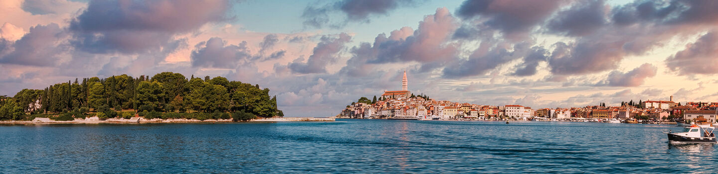 Blick von einem Boot auf Rovinj in Istrien, mit der Stadt im Hintergrund und einer ruhigen Abendstimmung, die den Himmel und das Wasser in sanfte Farben taucht.