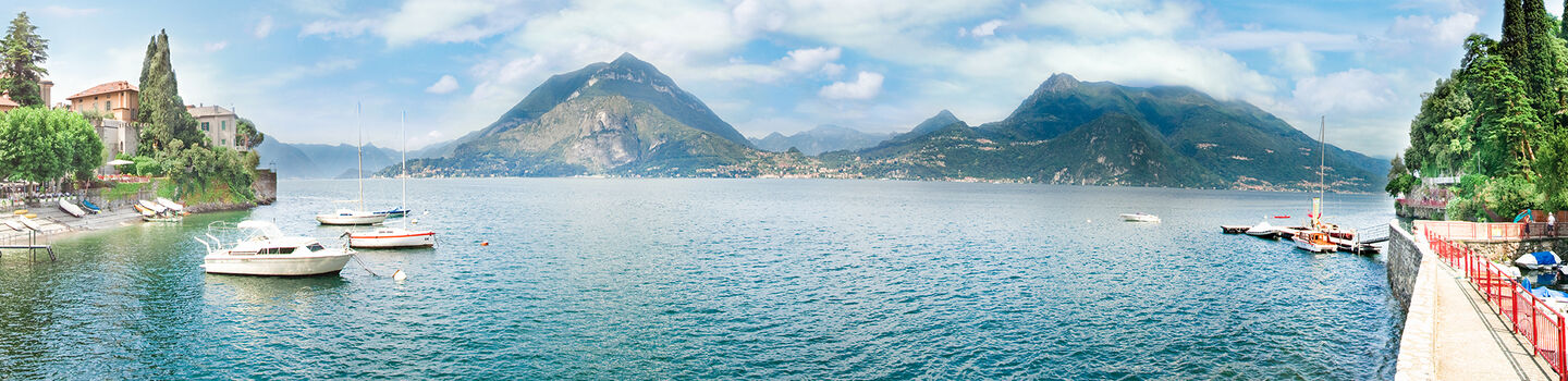 Ein malerischer Blick auf Varenna am Comer See, mit bunten Häusern an der Seite, ruhigem Wasser in der Mitte und majestätischen Bergen im Hintergrund.