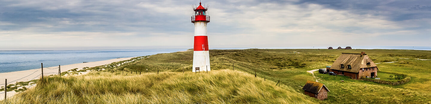  Leuchtturm auf der Insel Sylt, umgeben von weitläufigen Sanddünen und dem weiten, offenen Meer.