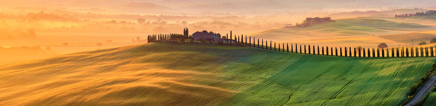 Ein malerischer Blick auf die toskanische Landschaft bei Sonnenaufgang, mit einem typischen Bauernhaus, sanften Hügeln und weitläufigen Weinbergen.
