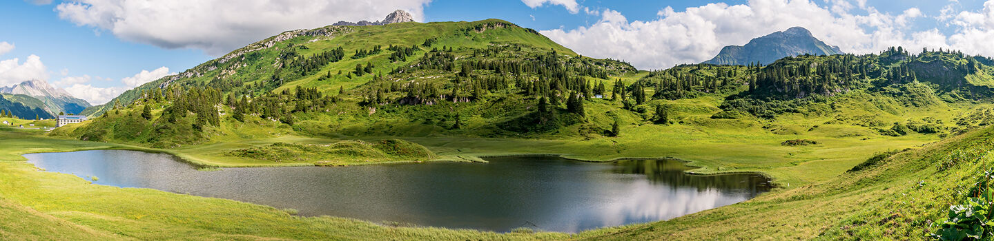 Ein idyllischer Wanderweg führt entlang eines kleinen Sees durch das robuste Lechquellen-Gebirge im Bregenzerwald in Vorarlberg.