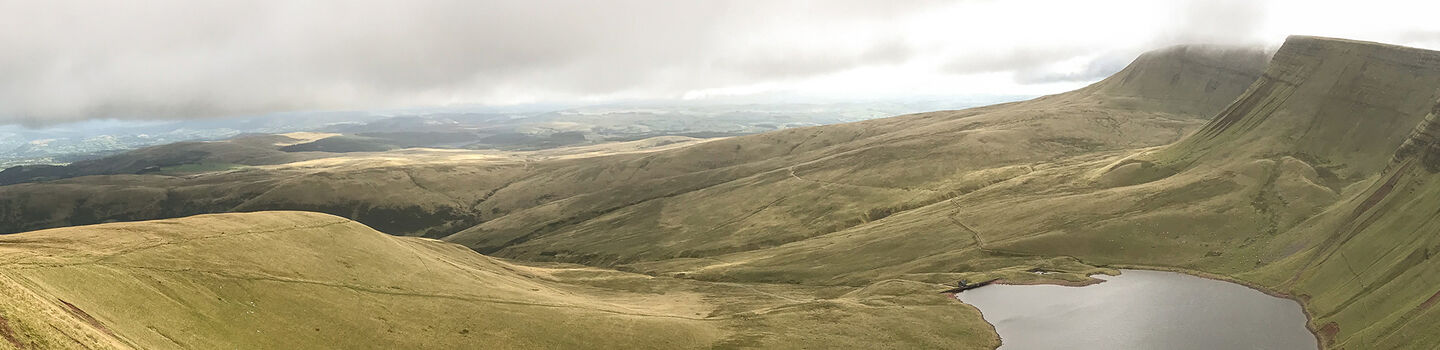Ein Panoramablick auf die sanften grünen Hügel und Berge der Brecon Beacons in Wales mit einem See im Vordergrund