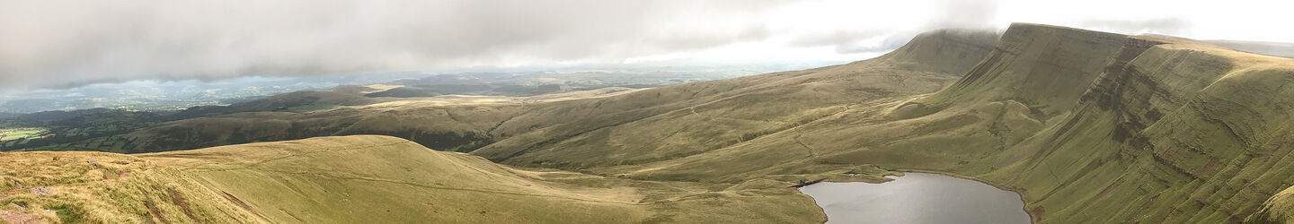 Ein Panoramablick auf die sanften grünen Hügel und Berge der Brecon Beacons in Wales mit einem See im Vordergrund iStock.com / 2checkingout