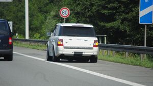 Ein weißer SUV steht am Pannenstreifen auf einer Autobahn, Geschwindigkeitsbegrenzung 80 km/h, 100m-Schild rechts.