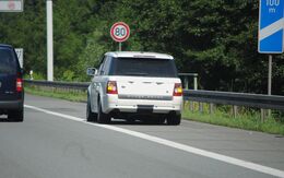 Ein weißer SUV steht am Pannenstreifen auf einer Autobahn, Geschwindigkeitsbegrenzung 80 km/h, 100m-Schild rechts.