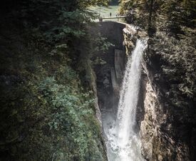 Das Foto zeigt eine Brücke über die Rappenlochschlucht. Auf der Brücke stehen Menschen und blicken auf den herabstürzenden Wasserfall.