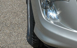 Rechter Vorderreifen und Scheinwerfer von einem silbernen Auto, das auf Asphalt steht, im Bild.