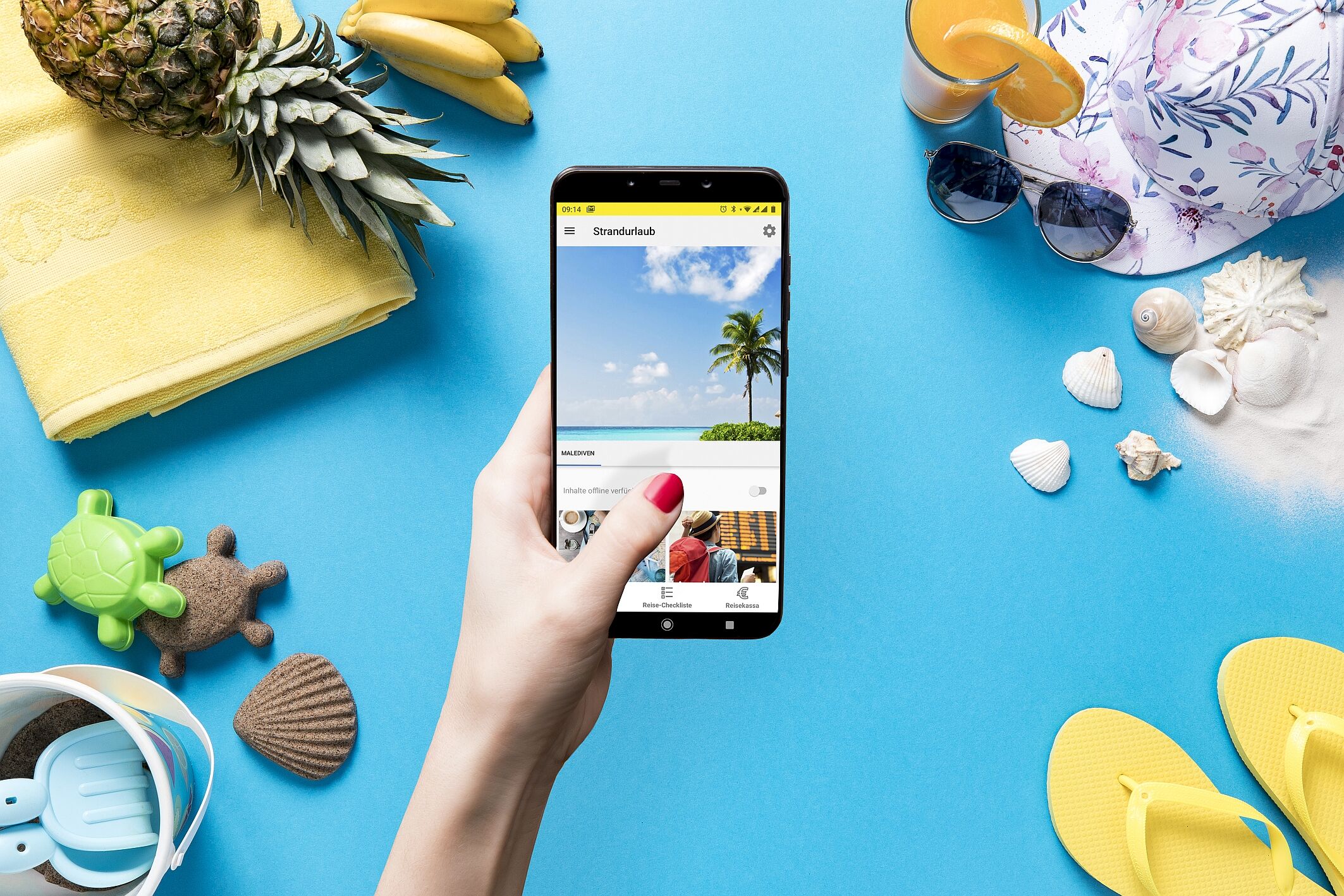 Eine Hand hält ein Smartphone mit einem Strandurlaubbild, umgeben von Sommerutensilien: Handtuch, Ananas, Sonnenhut, Sonnenbrille, Sandspielzeug, Muscheln und Flip-Flops.